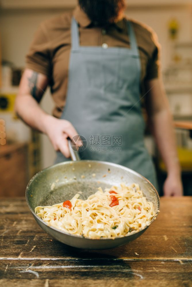 男厨师在木制房桌边端有通心粉和意面自制的fetucn烹饪传统的意大利菜准备过程图片