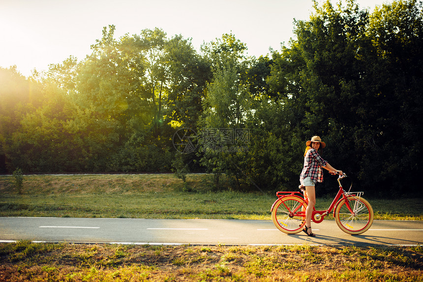 年轻女子骑着红色老式自行车在日落的夏日公园图片