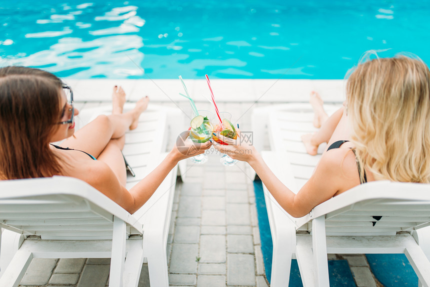 泳池边躺在躺椅上喝鸡尾酒的两个女孩图片