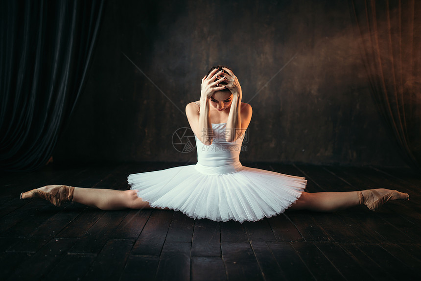 芭蕾舞表演伸展运动的柔软体白裙子的芭蕾舞女坐在黑色木制地板上的一根绳子图片