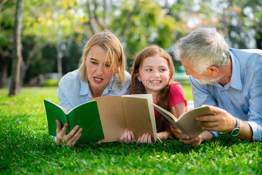 快乐的家庭一起阅读书本躺在公园绿草地上图片