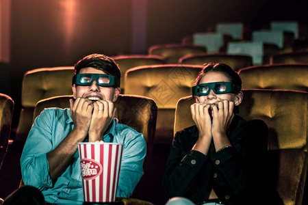 电影院里的男人和女观看一部3D眼镜的电影有兴趣观看屏幕奋和吃爆米花图片