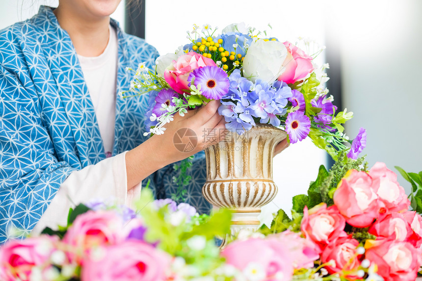 年轻女商人花卉店主在其商手工艺品和中制作或安排人工鲜花背心图片
