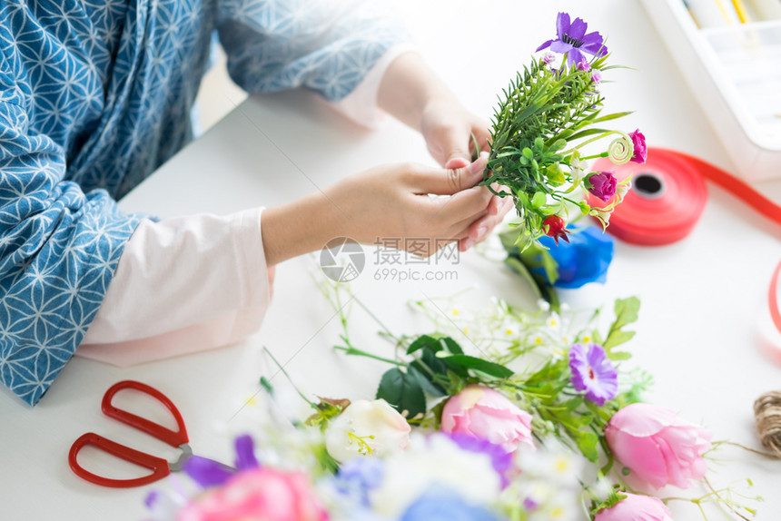 年轻女商人花卉店主在其商手工艺品和中制作或安排人工鲜花背心图片