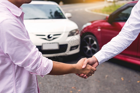 客户在车祸后同意就公路保险条款达成友好协议后与检查车祸主的汽保险代理商握手背景图片