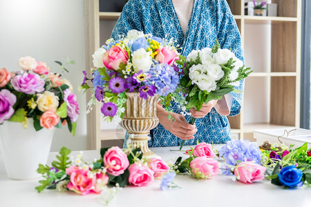 年轻女商人花卉店主在其商手工艺品和中制作或安排人工鲜花背心背景图片