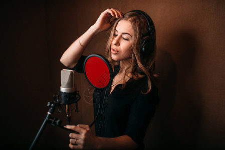在音乐室录歌的女手在反对麦克风的耳机中女唱家录音专业数字响技术图片