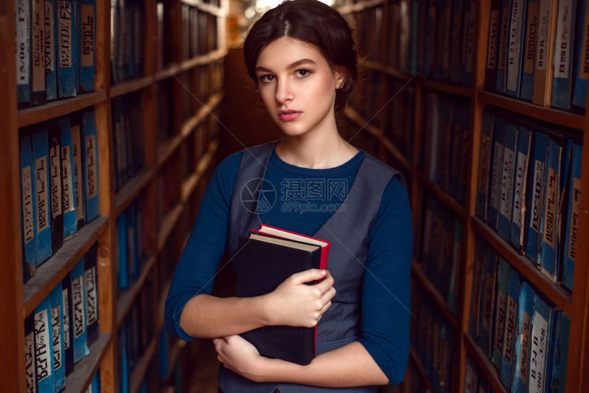 女学生在图书馆架之间抱着书图片