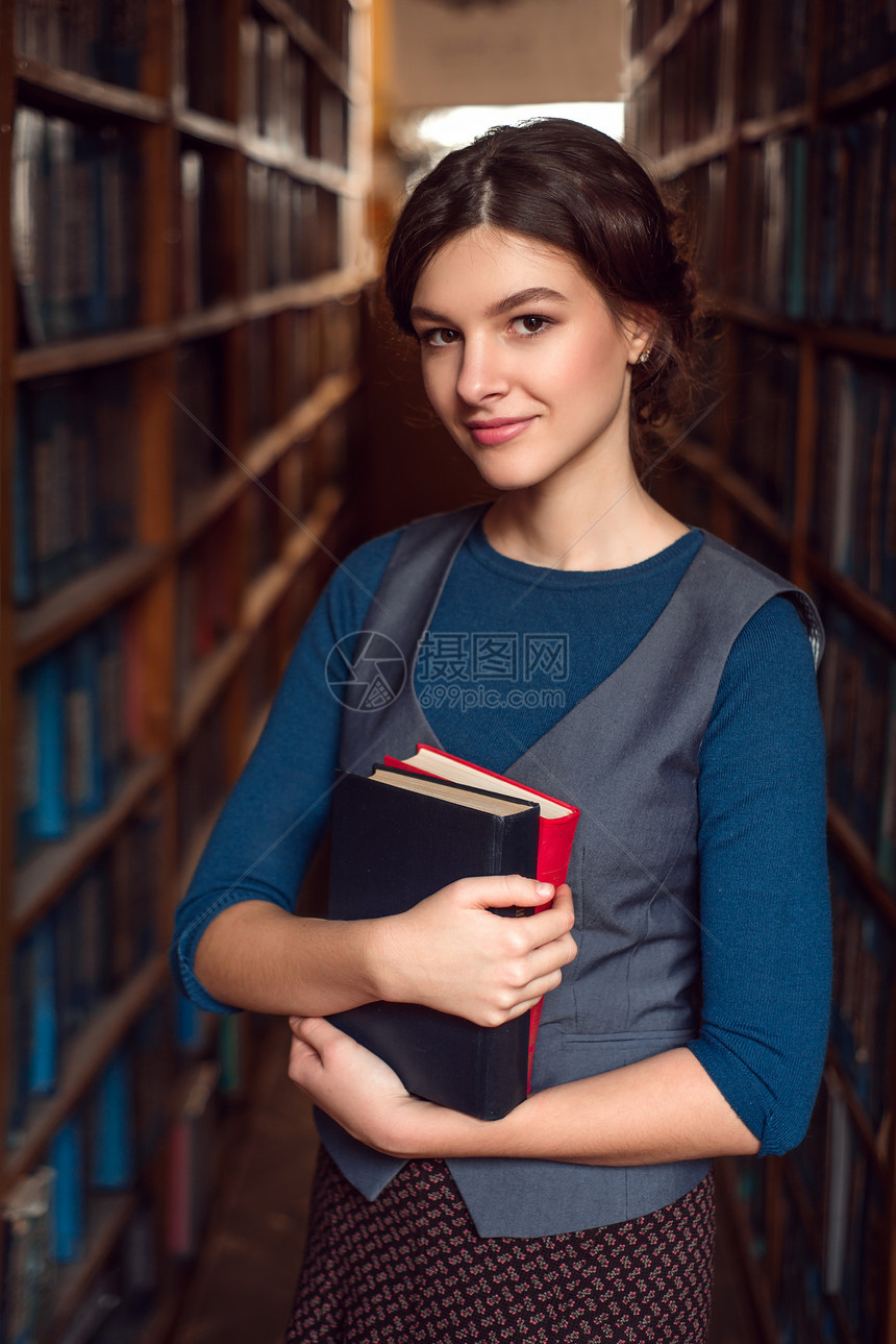 女学生在图书馆架之间抱着书图片
