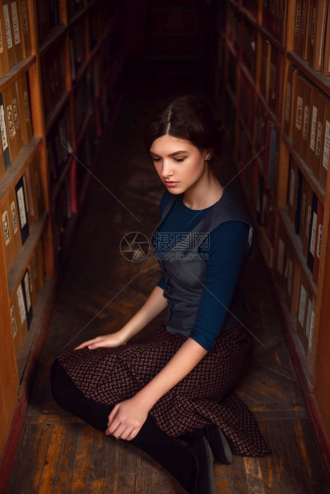 女学生在图书馆架之间坐着图片