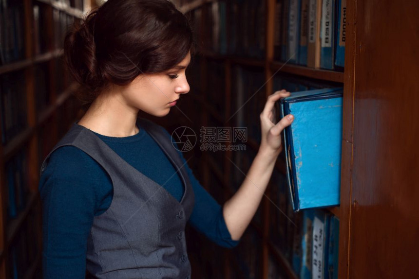 女学生在图书馆架之间挑选书图片