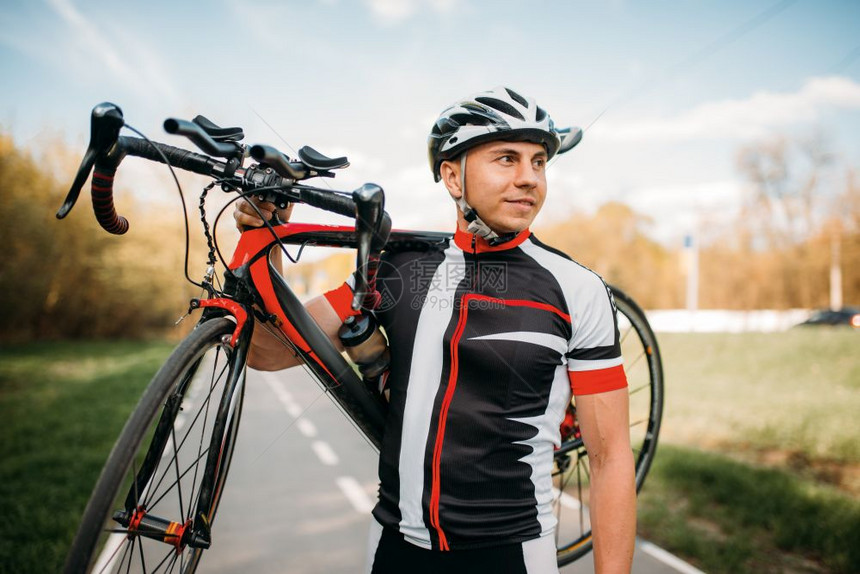 戴着头盔和穿着运动服的自行车运动员手扛自行车图片