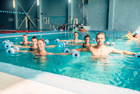 室内游泳池里有哑铃的女氧运动者和男教练水中有氧运动图片