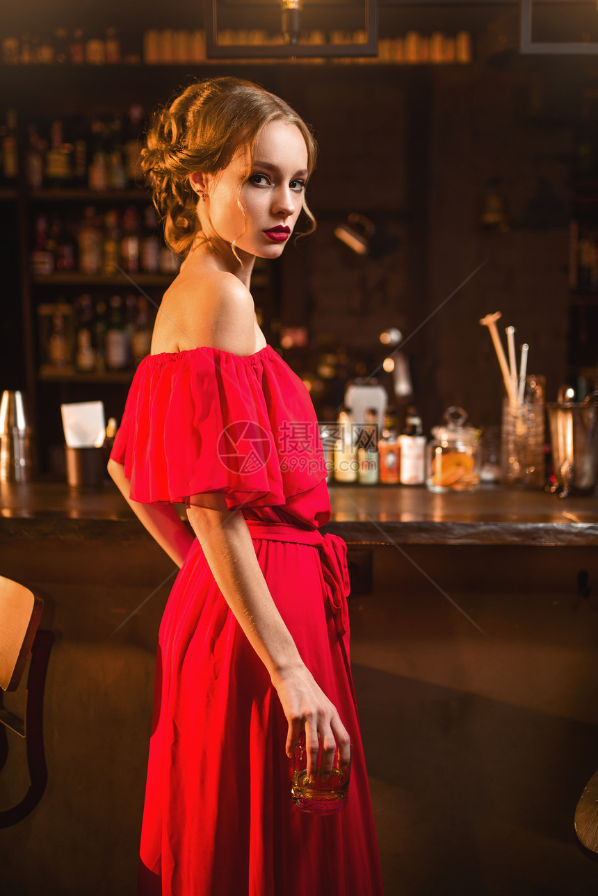 在酒吧柜台站着的穿红裙子年轻女士肖像图片