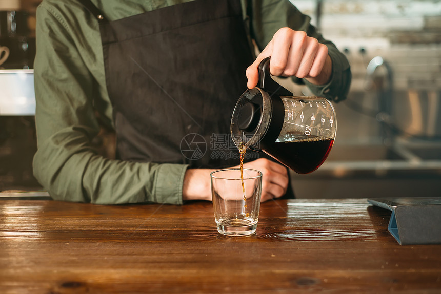 男酒保倒咖啡在玻璃杯中咖啡屋倒在背景上酒吧倒咖啡在玻璃杯中图片