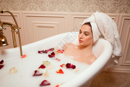 美丽的女人在充满玫瑰和花瓣的浴缸沐浴图片