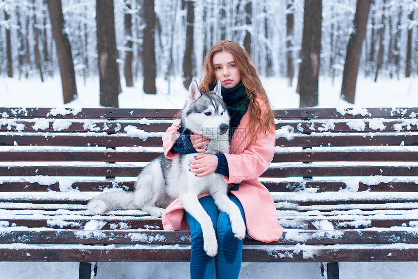 冬天美丽的女人抱着可爱的狗在外面的长凳上图片