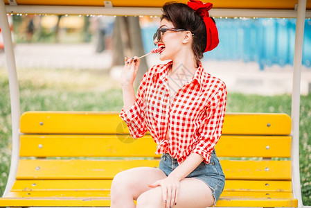 坐在公园的长椅上舔甜棒糖美国时尚的古老装背景图片