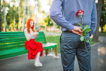男人偷偷送玫瑰给坐在公园长椅女友图片
