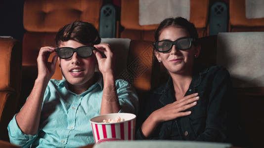 电影院里的男人和女观看一部3D眼镜的电影有兴趣观看屏幕奋和吃爆米花图片