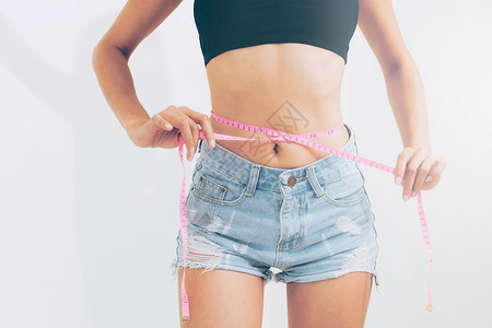 瘦弱的年轻女在吃完饭后用带子测量腰部瘦弱的女用带子测量腰部背景图片
