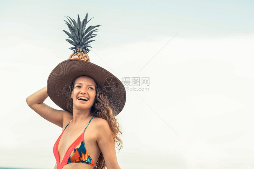 穿着泳衣拿着菠萝带着大太阳帽的快乐女子图片