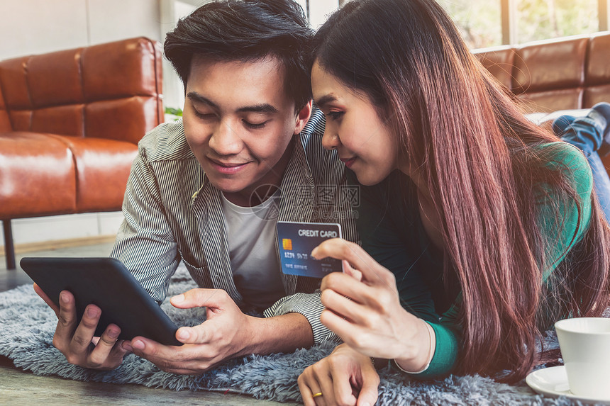年轻夫妇使用信卡在家中的互联网站上在线购物概念图片
