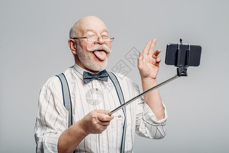 快乐的老人伸出舌头用手机自拍图片