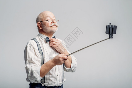 快乐的老人用手机做自拍灰色背景快乐的老人用手机做自拍图片