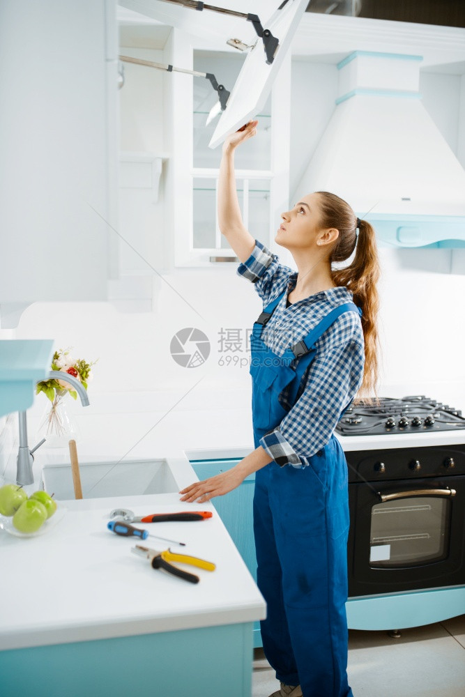 厨房中穿制服的修理橱柜中女家具制作人女清洁工修补装饰柜问题修理家庭服务穿制的修理橱柜中女家具制作人图片