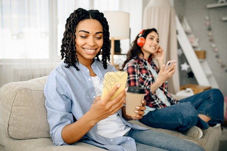 两个可爱的女人戴着耳机在沙发上听音乐喝咖啡图片