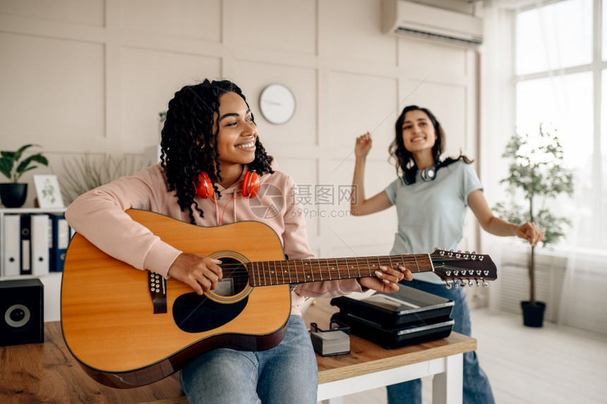 在家里弹吉他和听音乐漂亮的女友在房间里耳机放松声音情人在沙发上休息女朋友一起闲暇女人弹吉他和听音乐图片
