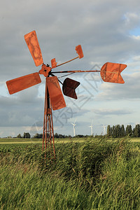 土牢中一只小鸡生锈的破碎风车和生锈的泵水其背景是现代风力涡轮机图片