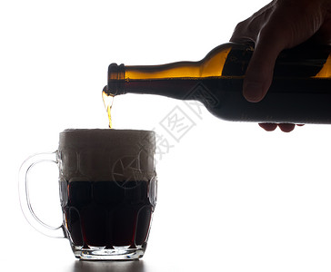 从棕色瓶子上倒满了黑杯啤酒并在液体上造成一大块泡沫图片
