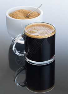 小玻璃杯中的黑咖啡和白碗中的糖的倒影图片