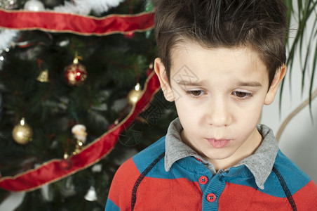 在圣诞节上不快乐的小男孩圣诞树在背景中图片