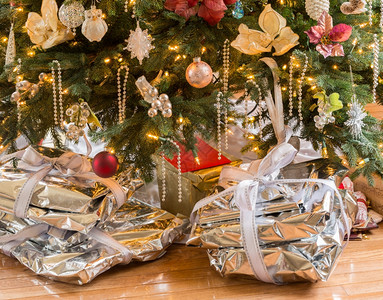 用银纸和丝带包裹的银质礼物在木地板上的圣诞树下图片