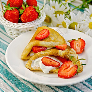煎饼加草莓和奶油一篮子浆果花朵在条纹的餐巾纸上图片