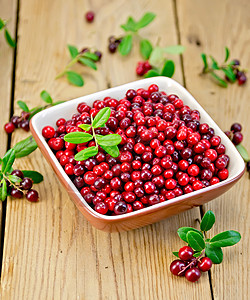 一碗熟的红色兰边莓碗里有一盆浆果和木板背景上的叶子图片