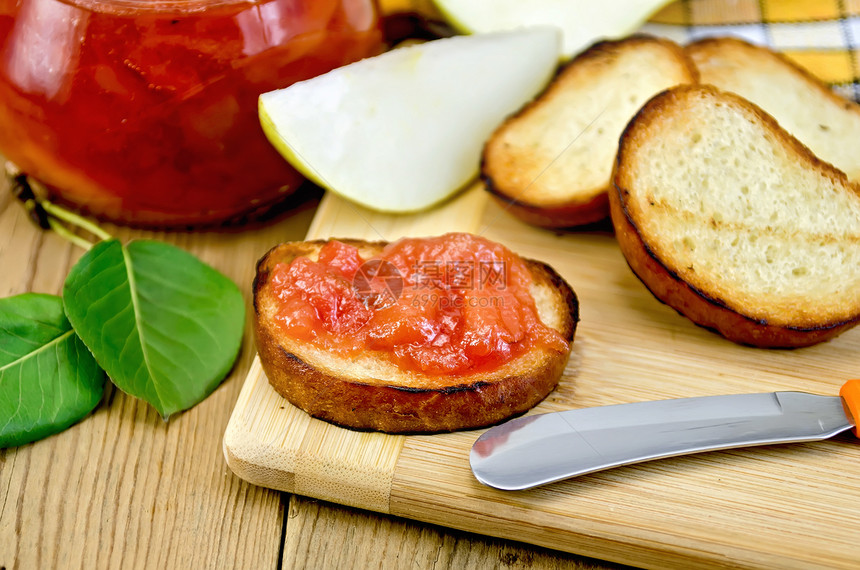 烤面包片一个加梨果酱的玻璃罐背景木板上的刀图片