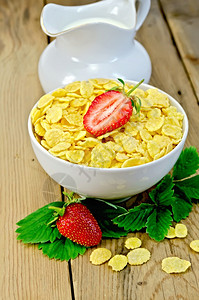 白碗中的玉米片叶子和草莓木板背景的罐头中牛奶图片