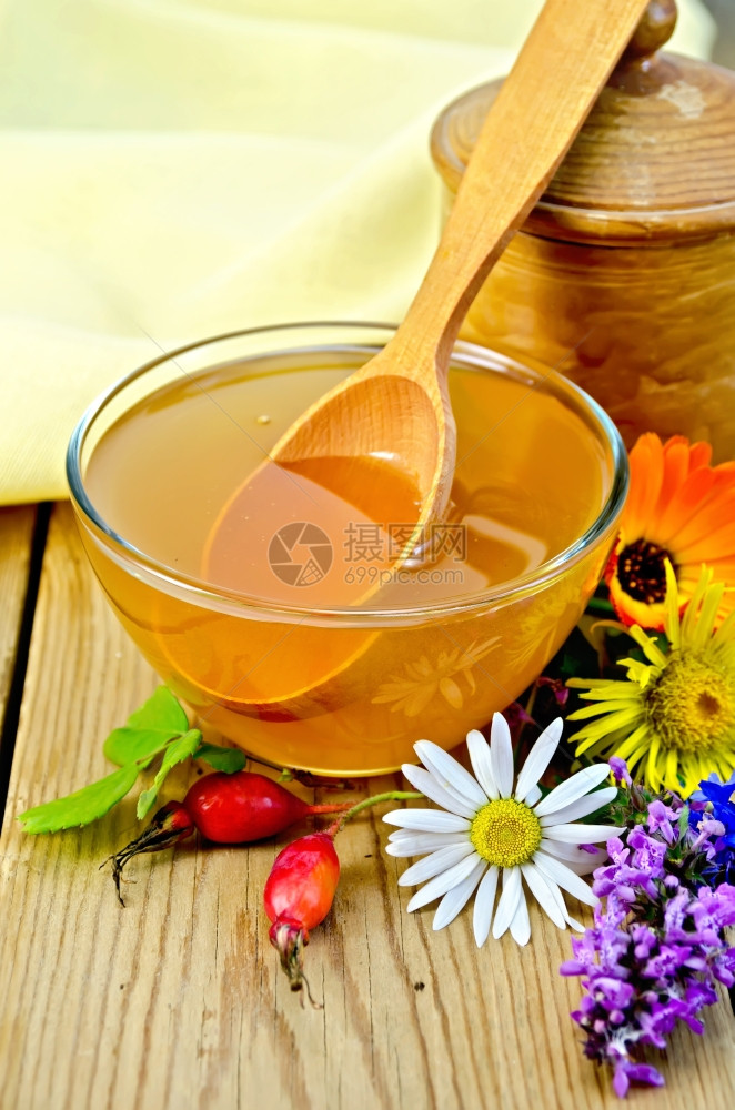 蜂蜜在玻璃碗和木锅勺子玫瑰果鲜花木板背景上的餐巾纸图片