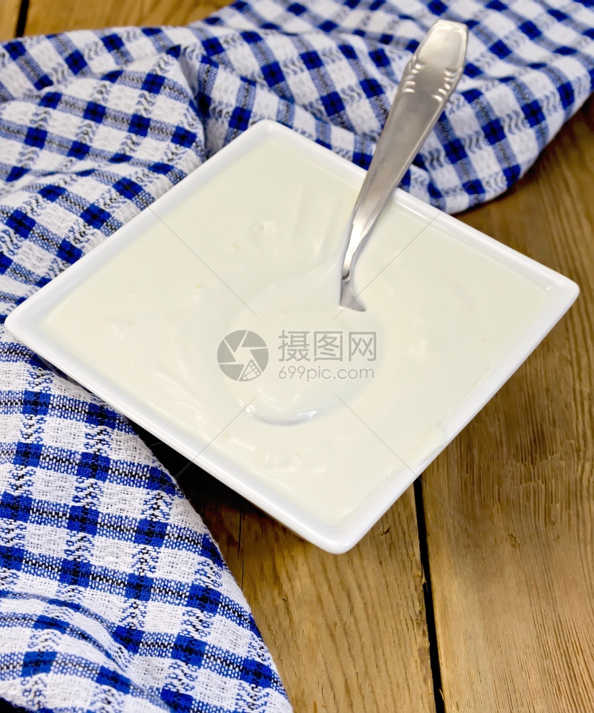 白方碗中的酸奶油蓝彩餐巾纸木板上的勺子图片