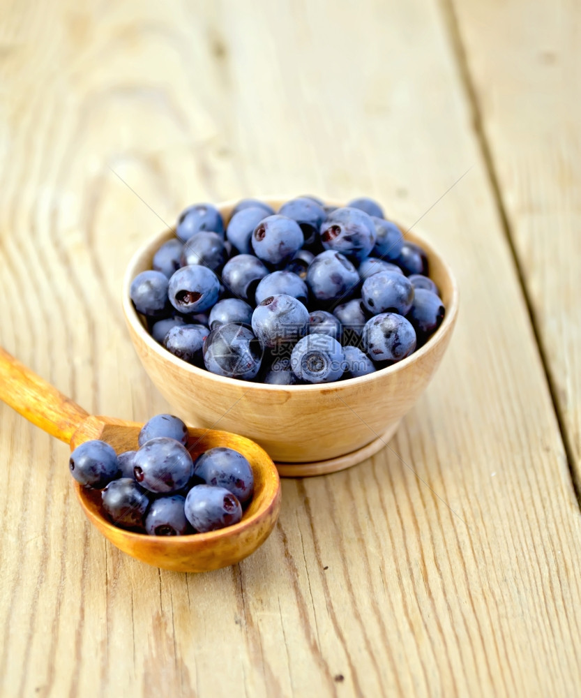 蓝莓放在木碗里勺子放在木板上图片