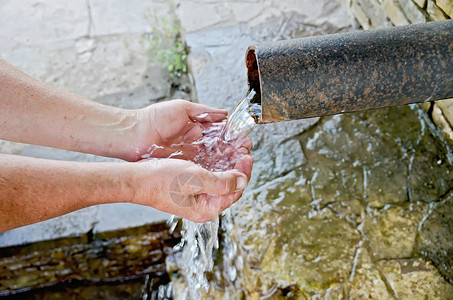 泉水从管子流进石底下人手背景图片
