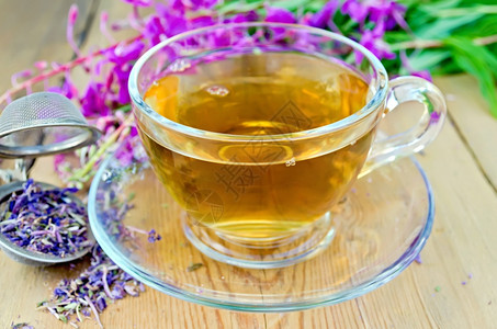 玻璃杯中的草药茶用干鲜花的金属筛子火草木板上的青鲜花图片