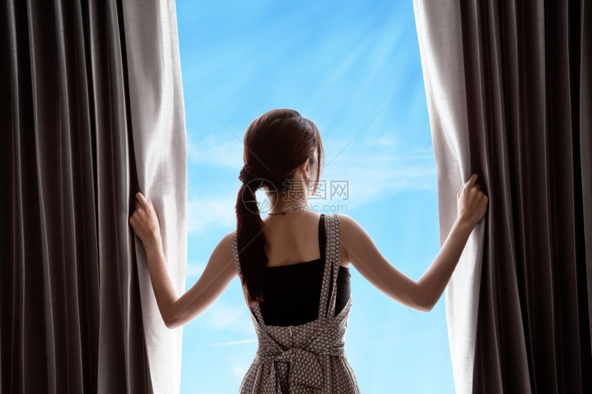 年轻妇女打开窗帘和蓝天图片