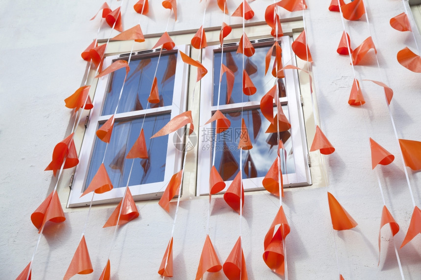 沿着白色墙壁和反映蓝天空的窗口横线排列橙旗图片