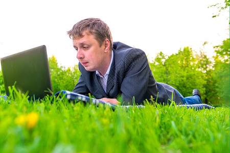 躺在草坪上用笔记本电脑工作的男子图片