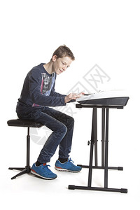 坐在白色背景里学习电子钢琴的青少年男孩图片